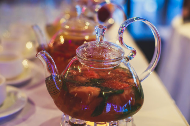 美丽温暖的图片透明茶壶茶壶与可口的红茶与苹果，柠檬和姜在桌子上蜡烛和甜点的背景图片下载