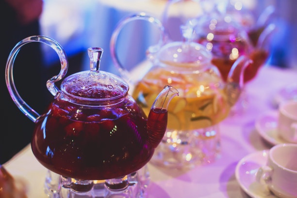 美丽温暖的图片透明茶壶茶壶与可口的红茶与苹果，柠檬和姜在桌子上蜡烛和甜点的背景图片下载