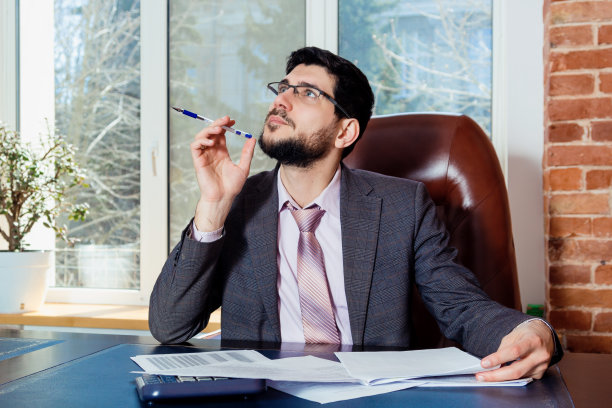 一个年轻人坐在办公室的办公桌前处理文件。图片下载