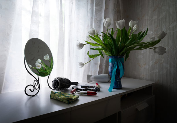 镜子、郁金香、梳子和女士化妆品放在房间靠窗的梳妆台上。图片下载