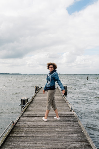 一个阴天的夏天，穿着休闲的女人站在木栈桥上。自由的概念素材图片