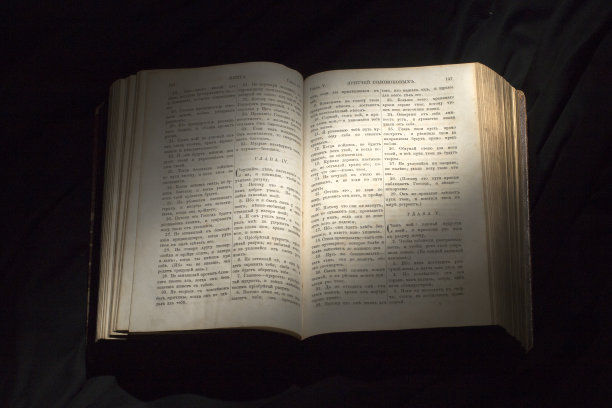 打开书，用灯光照亮文本。开卷阅读教育读者。在黑色背景上阅读古代圣经文本。俄罗斯《圣经》图片下载