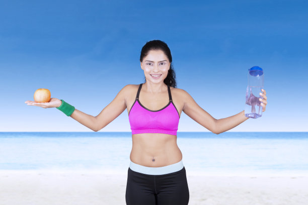 在海滩上拿着苹果和瓶子的运动型女人图片下载
