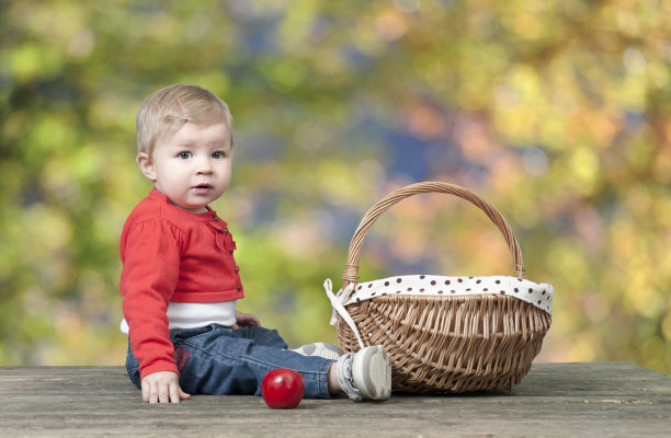 婴儿抱着一篮子苹果，放在一张旧木桌上图片下载