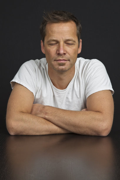 中年男子双臂交叉，在黑色背景下闭眼图片下载