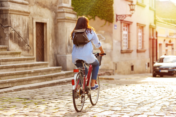 后视图的年轻女子骑自行车沿街道在日落。图片下载
