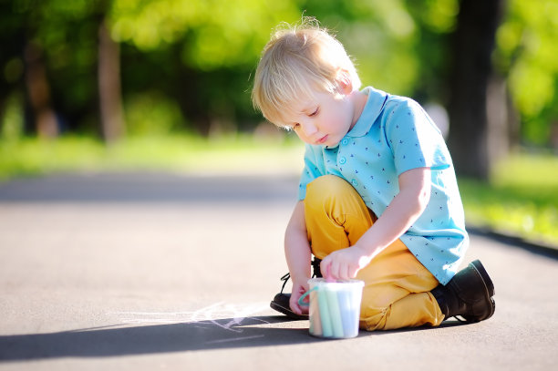 一个全神贯注的小男孩坐在沥青上用彩色粉笔画画图片下载
