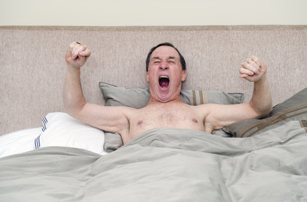 瞌睡的老年人打哈欠和伸展在床上图片下载