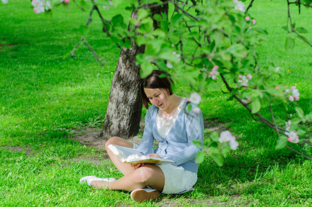 年轻女子在盛开的树下看书图片下载