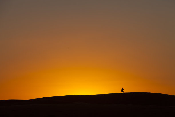夕阳下，一个柏柏尔人在沙丘上行走的剪影图片下载
