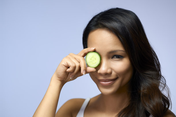 女孩拿着一片黄瓜遮住一只眼睛图片下载