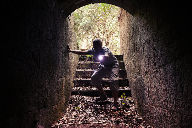 年轻人拿着手电筒进入黑暗的石头隧道图片下载