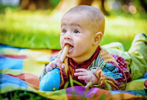 可爱的小男孩咬着一个木制玩具图片下载