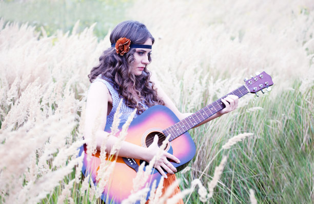 嬉皮女孩拿着吉他在草地上走图片下载