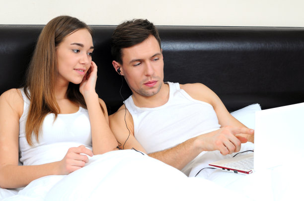 一对夫妇在床上放着笔记本电脑图片下载