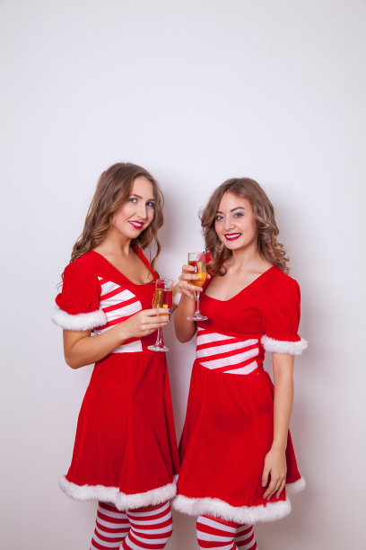 美丽快乐的两个女人穿着圣诞老人的衣服，喝着香槟图片下载