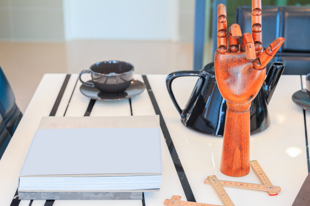 客厅的桌子上放着一本书、咖啡杯、黑壶和一只木手。图片下载