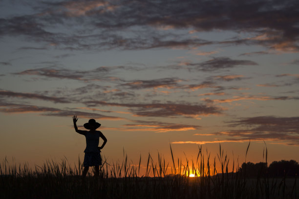 黄昏时分，一位女士向夕阳挥手的剪影。图片下载