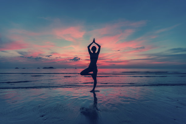 日落时分，年轻女性在海滩上练习瑜伽图片下载