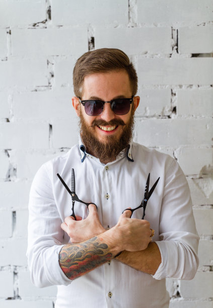 微笑的年轻胡子理发师与一对黑色剪刀图片下载