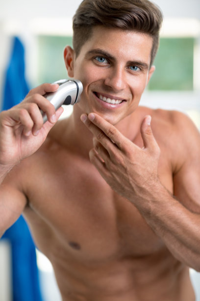 英俊的年轻人用电动剃须刀刮胡子图片下载