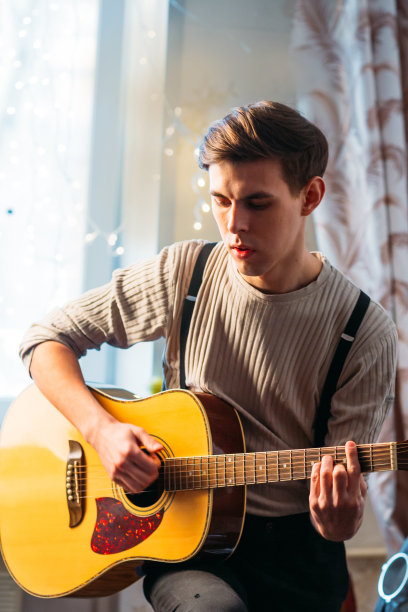 一个年轻人坐在家里弹吉他图片下载