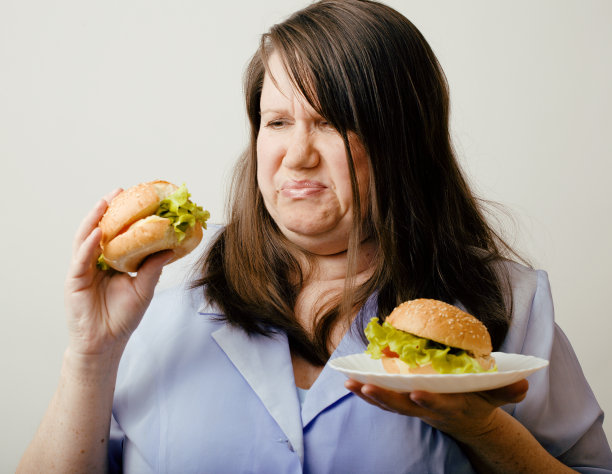胖女人在汉堡包和沙拉中选择图片下载