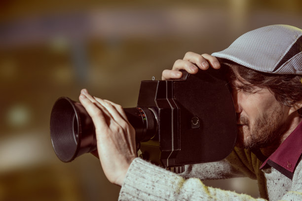 戴着一顶帽子的男人，手里拿着一台旧摄像机图片下载
