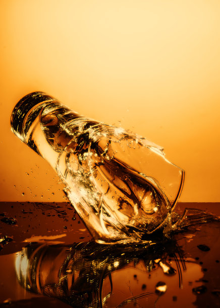 在橙色的背景下，玻璃杯爆裂，水碎裂。图片下载