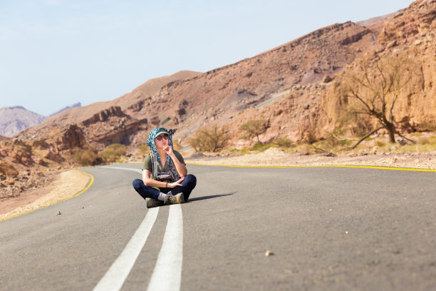 年轻女子坐在沙漠柏油路上。角度的观点。图片下载