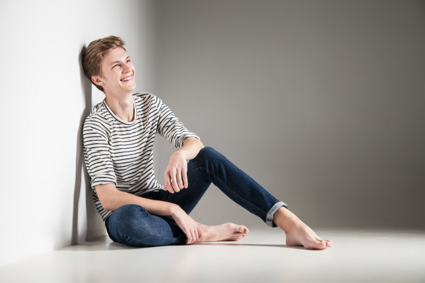 漫不经心的年轻人摆姿势在地板上微笑过灰色图片下载