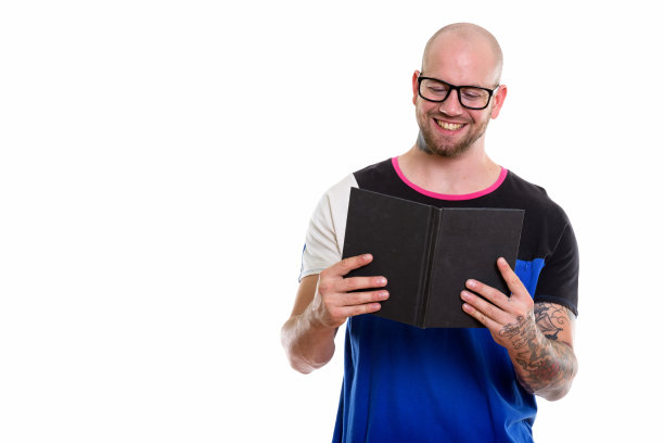 工作室拍摄的年轻快乐的秃头肌肉男微笑着读书素材图片