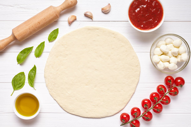 披萨的准备。厨房桌上的烘焙材料:面团、马苏里拉奶酪、番茄沙司、罗勒、橄榄油、番茄、奶酪、香料。图片下载
