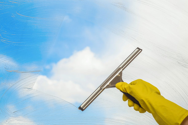 手戴黄色防护手套，用专业清洁刷清洗窗户。早春的窗户在蓝天的背景下清洁。保洁清洁窗户。素材图片