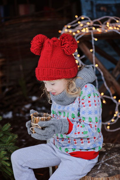 穿着圣诞毛衣的小女孩坐在户外，拿着烛台图片下载