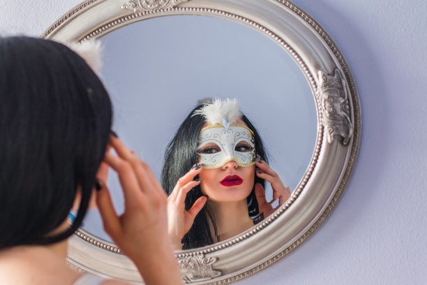 神秘的年轻女子戴着狂欢节面具站在镜子前图片下载