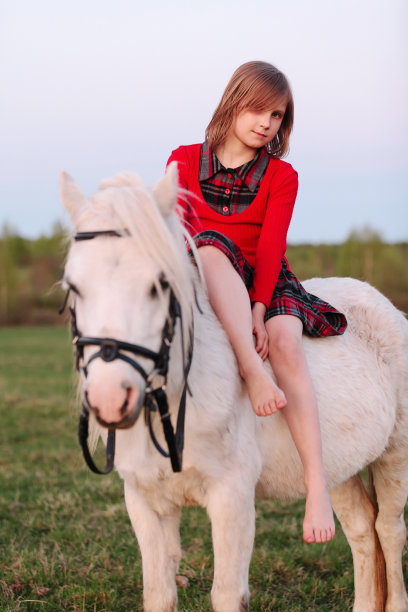 小女孩骑在白马上，面带微笑图片下载