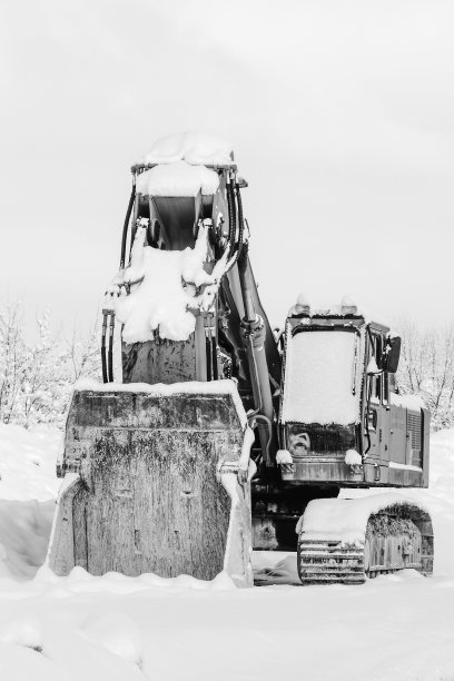 挖掘机站在雪地里的冬天，靠近户外。失业问题的概念。黑白照片图片下载