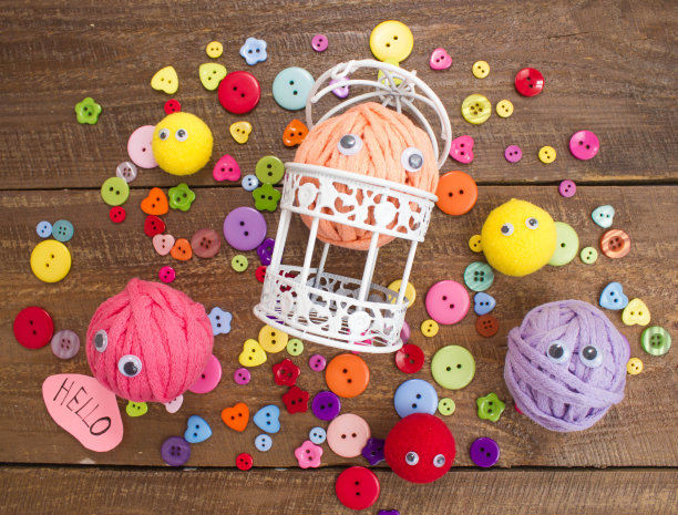 有眼睛和彩色纽扣的有趣的毛线团。图片下载