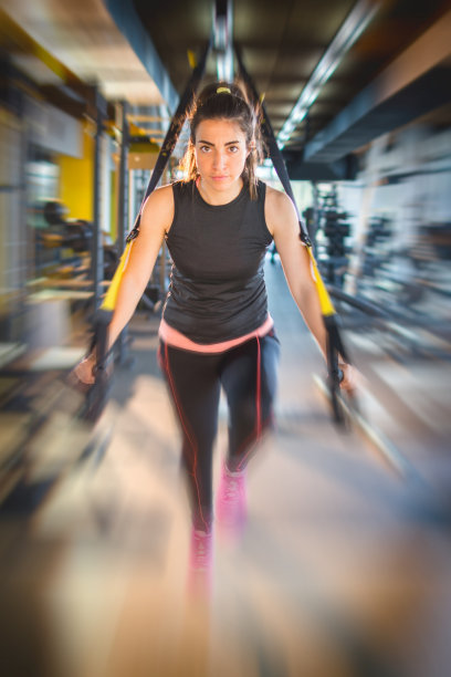 运动女性在健身房用吊带做手臂运动。运动效果模糊。图片下载