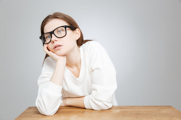 无聊的戴着眼镜的少女坐在桌边图片下载