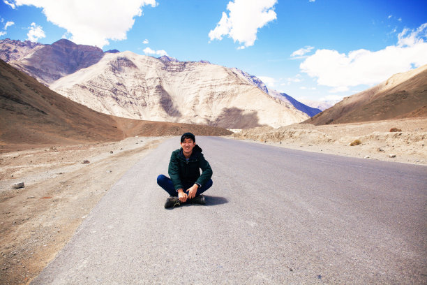年轻的亚洲男性旅行者坐在空旷的马路中间图片下载