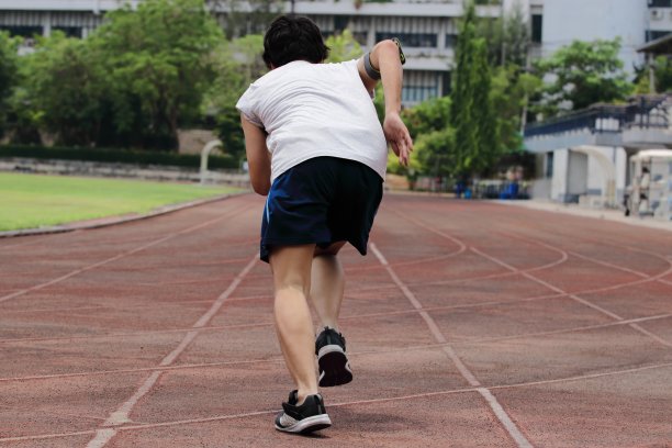 后视图年轻的亚洲短跑运动员离开开始在田径运动场的跑道。图片下载