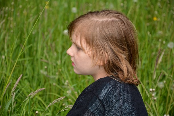 女孩坐在绿色的草地上，往旁边看图片下载