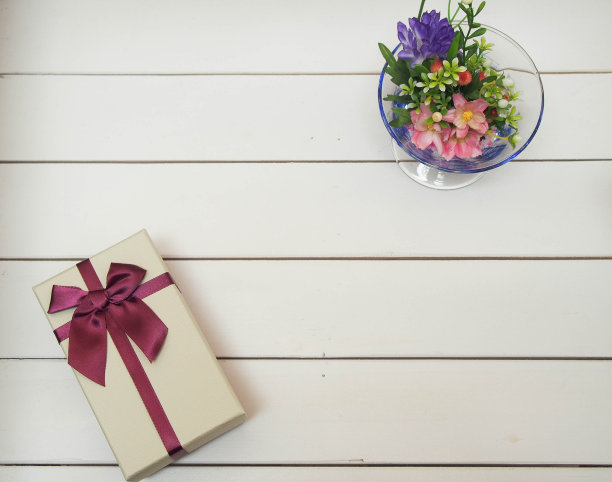 白色木桌上系着丝带的礼品盒。花瓶里插着花图片下载
