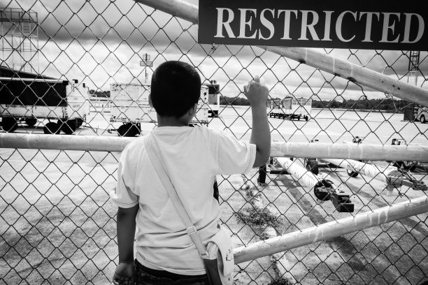 小亚洲男孩悲伤地独自站在机场门口，黑白相间的色调图片下载