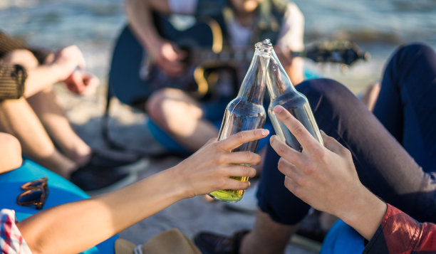 手在海滩上碰杯啤酒瓶的特写图片下载