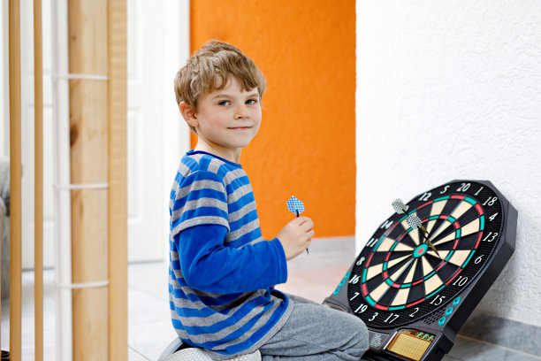 可爱的金发幼儿园小男孩在室内玩飞镖。图片下载