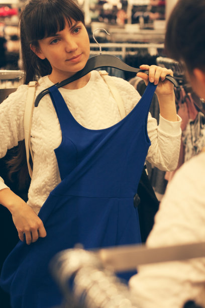 女孩在服装店的镜子前试穿蓝色的衣服。图片下载