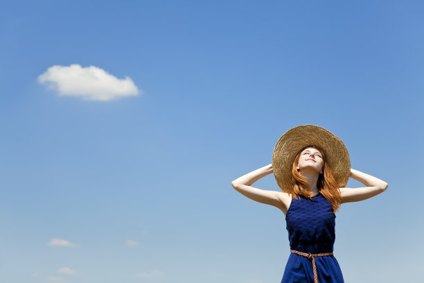 红发女孩在春天的蓝天背景。图片下载